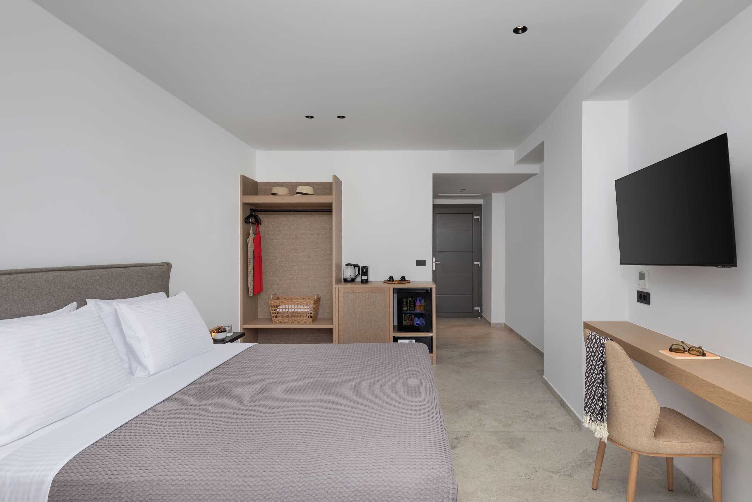 A modern hotel room with a bed, a desk, a chair, a TV, and a wardrobe.