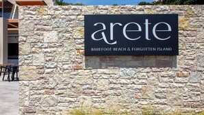 Un muro de piedra con un letrero que dice "Arete Barefoot Beach & Forgotten Island".