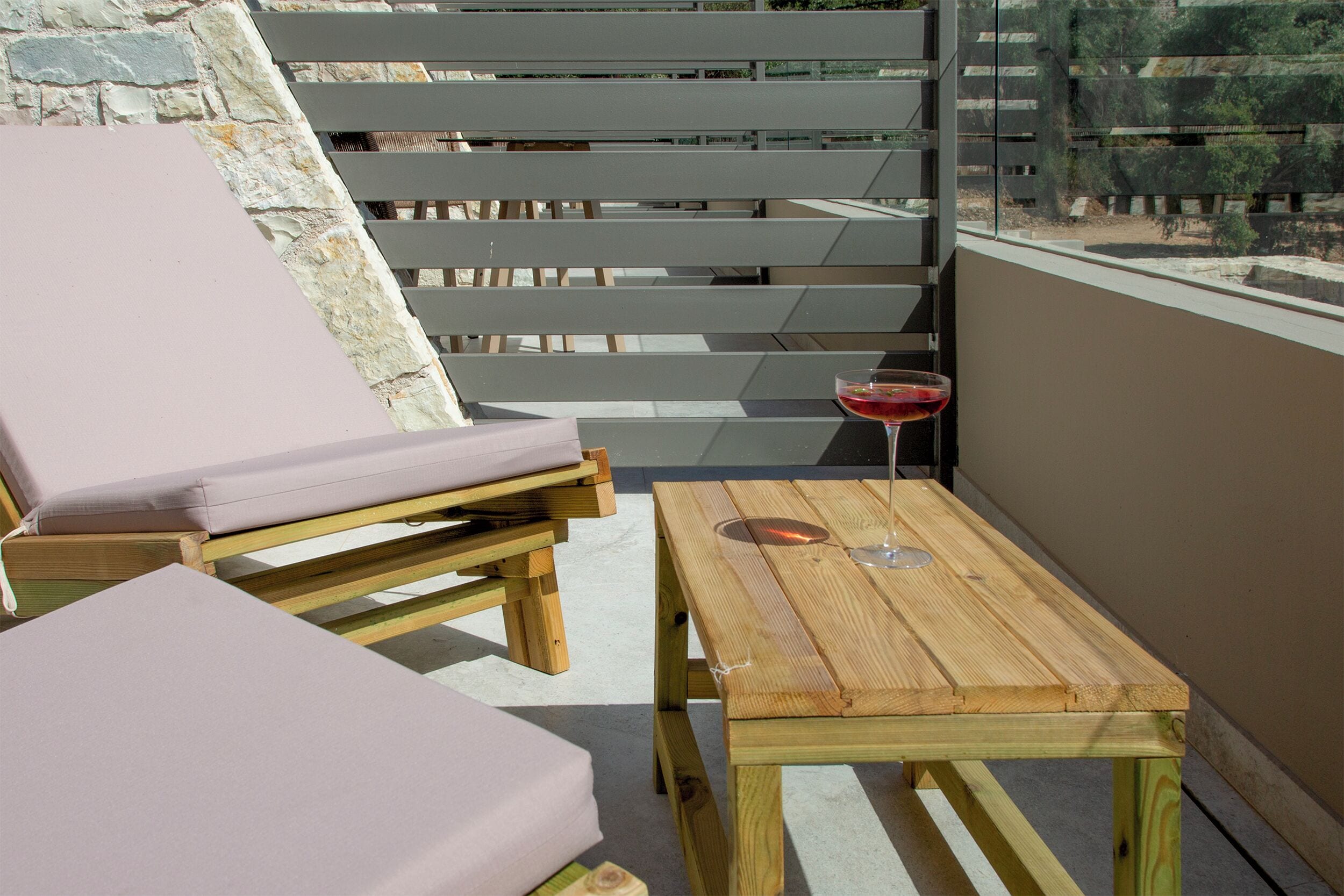 Un balcón con mobiliario de madera, incluyendo una mesa y dos sillas con cojines, y una copa de vino tinto sobre la mesa.