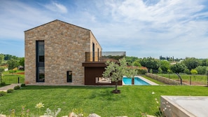 A modern stone building with a large window, a swimming pool, and a well-maintained lawn.