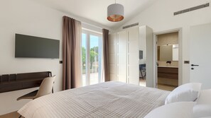 Camera d'albergo con un letto, una scrivania, una TV e un bagno visibile attraverso una porta aperta.