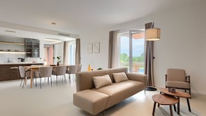 A modern living room with a sofa, dining area, and a view of a swimming pool.