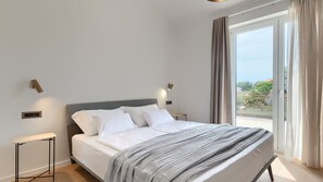 Une chambre à coucher avec un lit, des tables de chevet, une fenêtre avec des rideaux et une vue sur l’extérieur.