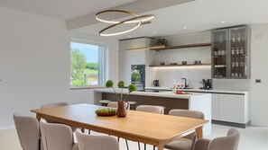 Une cuisine moderne avec un îlot central, une table à manger avec des chaises et une vue sur la verdure à l’extérieur.
