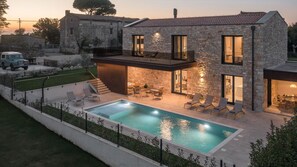 Une maison en pierre à deux étages, dotée d’une piscine, d’un espace salon extérieur et d’un escalier menant à l’étage supérieur.