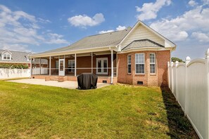 A single-story brick house with a covered patio, a lawn, and a white picket fence.