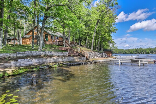 A log cabin with a dock extending into a lake, surrounded by trees and a stone wall. - Estrold's Resort- Birch Cabin (St. Germain)