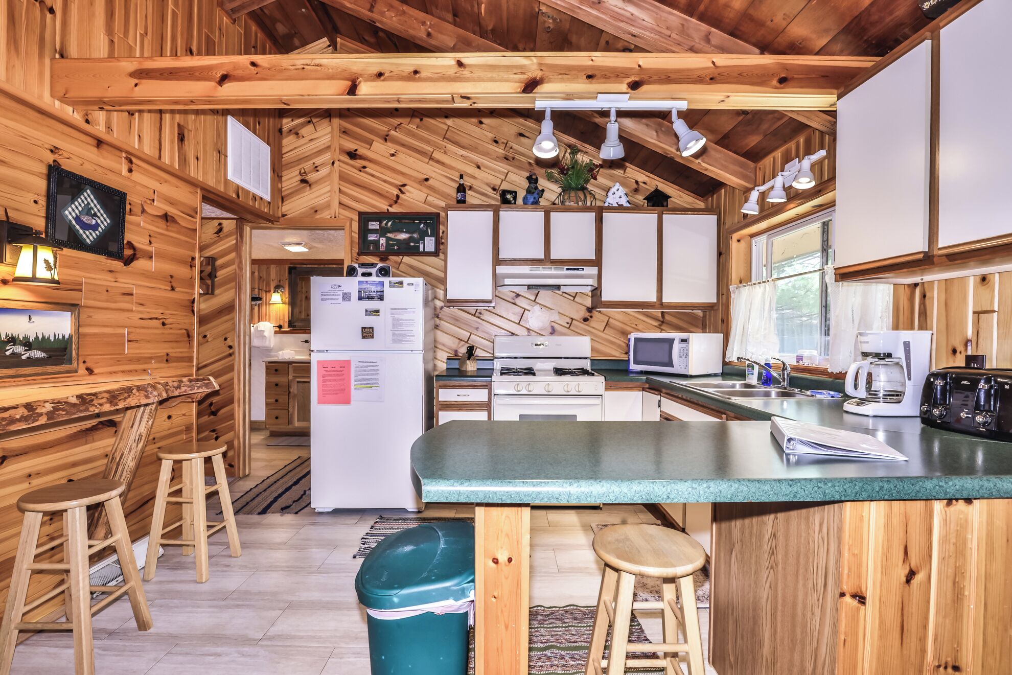Une cuisine chaleureuse, aménagée dans le style d’un chalet, avec des murs en bois, un îlot central, des tabourets de bar et des appareils électroménagers de base.