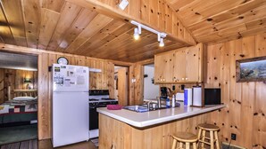 A cabin interior with a kitchen area featuring a refrigerator, stove, and bar stools. - Estrold's Resort- Driftwood Cabin (St.Germain)