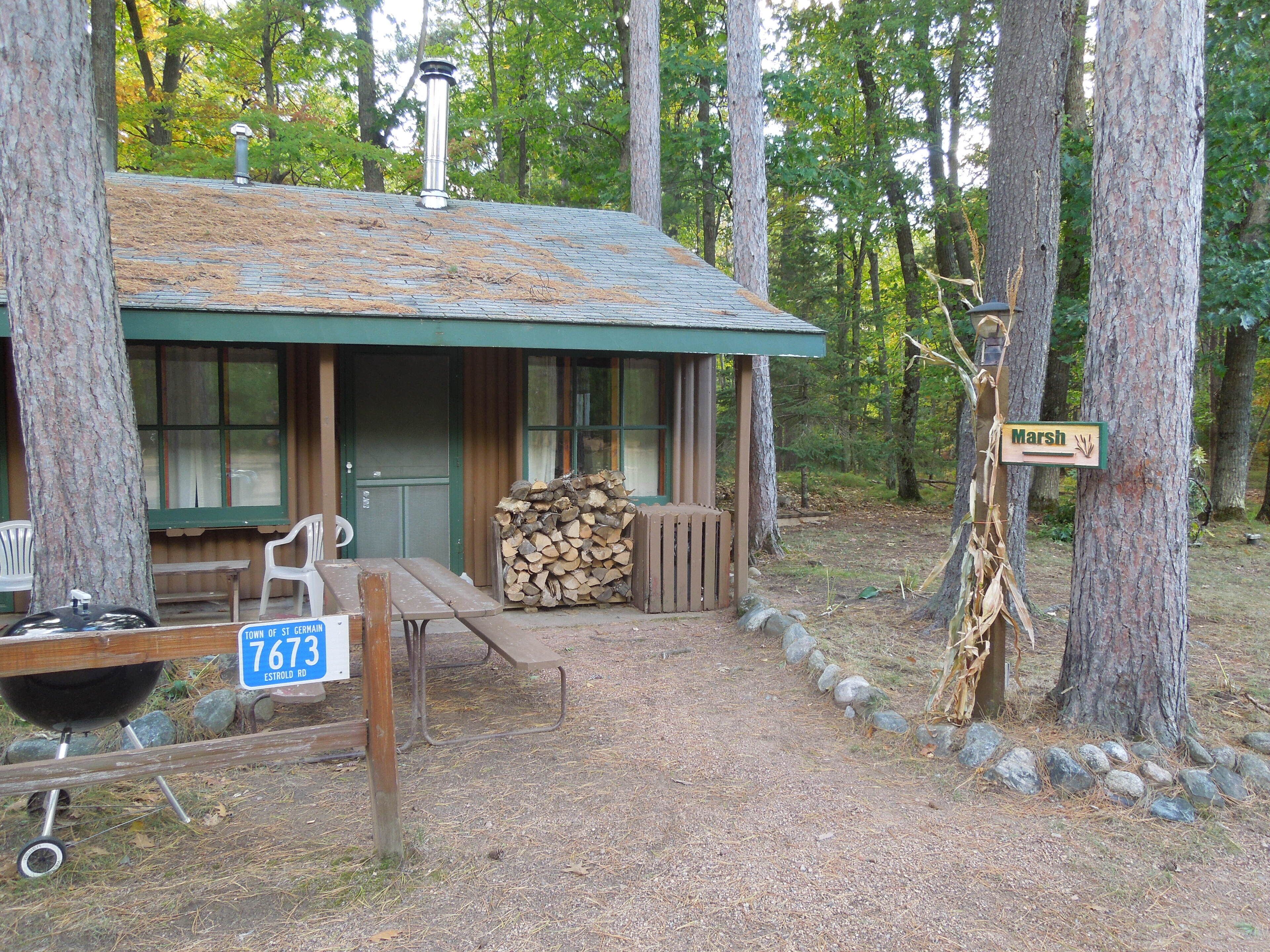 A rustic cabin with a green roof, a wooden deck, and a sign indicating 'Marsh'.