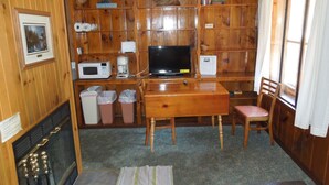 L’intérieur chaleureux d’un chalet, avec un revêtement mural en bois, un téléviseur, une machine à café et une cheminée.