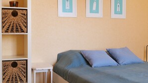 Een slaapkamer met een bed, twee kussens, een nachtkastje en drie foto’s van vuurtorens, bevestigd aan de muur.
