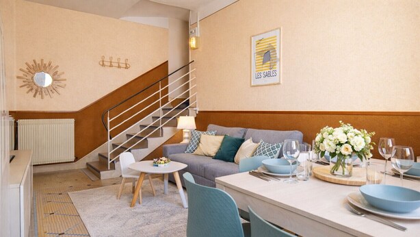 Een moderne woonkamer met een trap, een eetgedeelte met blauw servies en een kunstwerk in een lijst aan de muur.