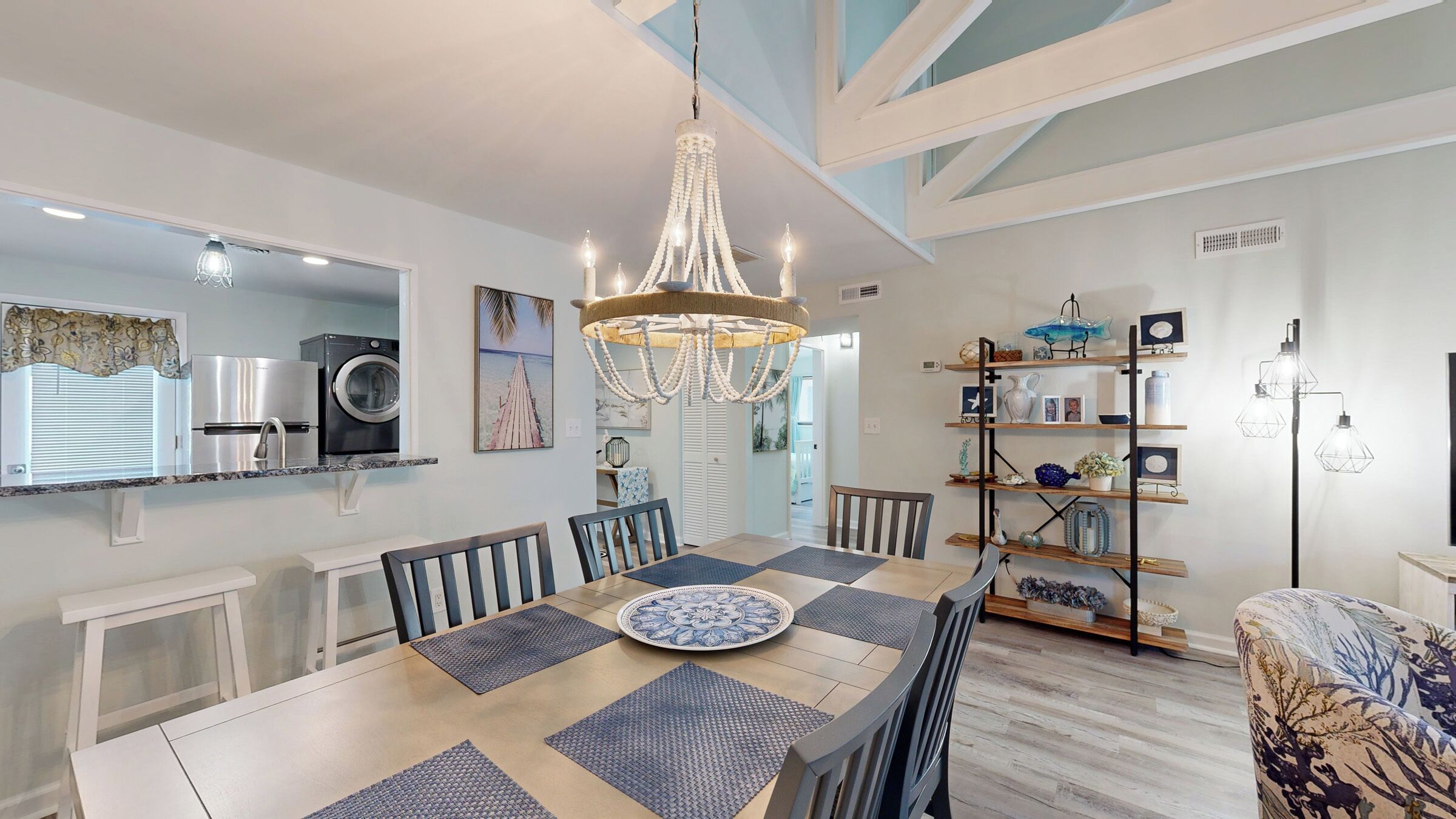 Una cocina moderna con lavadora integrada, un comedor con candelabro y una sala de estar con estantería.