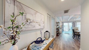 A spacious room with a large painting, a wooden bench with a blue and white patterned tablecloth, and a view of a balcony with outdoor furniture.