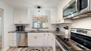 A modern kitchen with white cabinetry, a granite countertop, a built-in microwave, and a stainless steel oven.