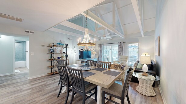 A spacious dining area with a high ceiling, a chandelier, and a view of the adjacent living room.