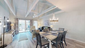 A spacious dining area with a high ceiling and natural light, a cozy living room with a sofa and coffee table, and a view of the backyard through a sliding glass door.