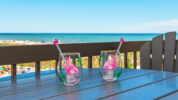 Two glasses with flamingo designs on a wooden table with a view of the beach and ocean. - Oceanfront Building With Great Ocean and Bay Views (OCEAN OCEAN CITY)