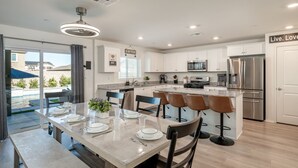 A modern kitchen with white cabinets, stainless steel appliances, and a central island with bar stools. - Entertainer`s Paradise | Luxe Pool + Game Room (Coachella)
