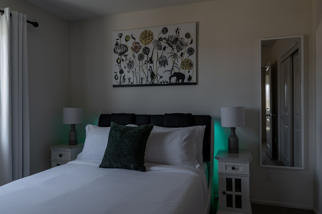 Une chambre d’hôtel comprenant un lit, deux tables de chevet avec des lampes, une grande œuvre d’art murale et un miroir.