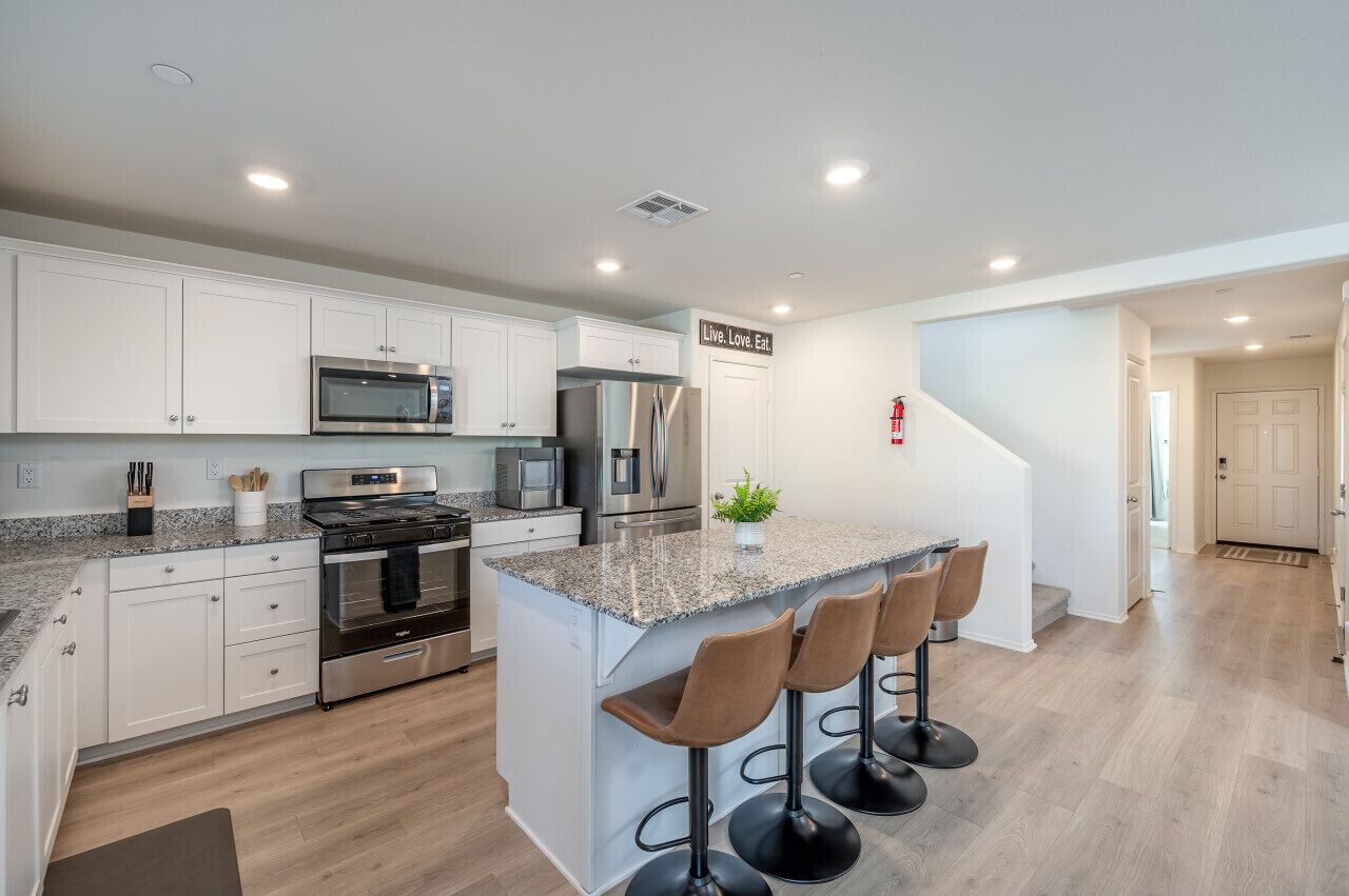 A modern kitchen with white cabinets, stainless steel appliances, a granite countertop, and a central island with bar stools.