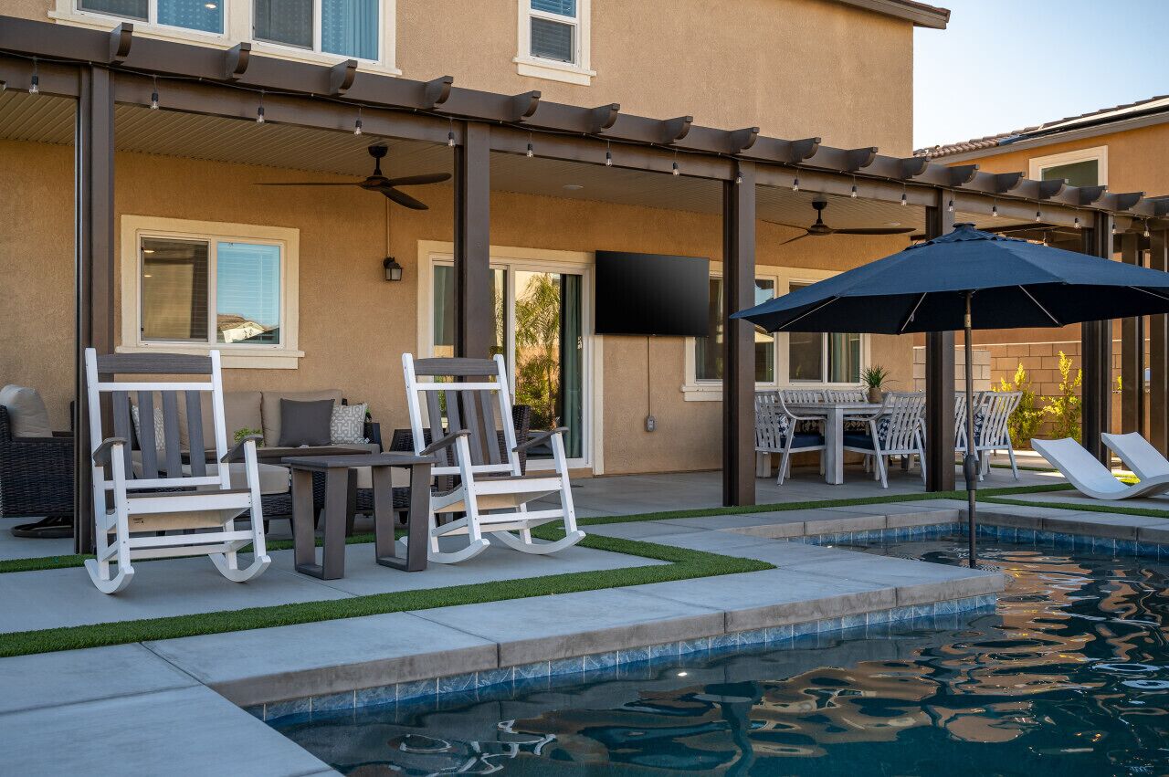 Eine überdachte Terrasse mit Gartenmöbeln, einem Pool und einer Pergola mit Deckenventilatoren.