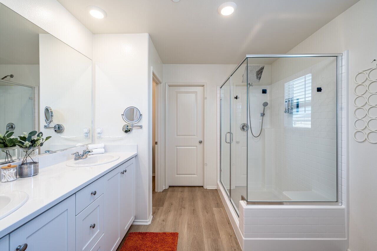 A modern bathroom with a glass-enclosed shower, white vanity with dual sinks, and a large mirror.