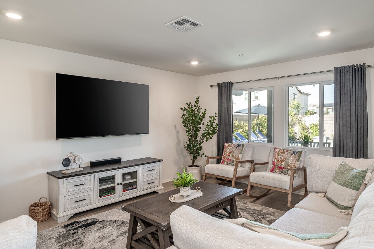 A modern living room with a flat-screen TV, a white cabinet, two chairs, a sofa, and a coffee table.