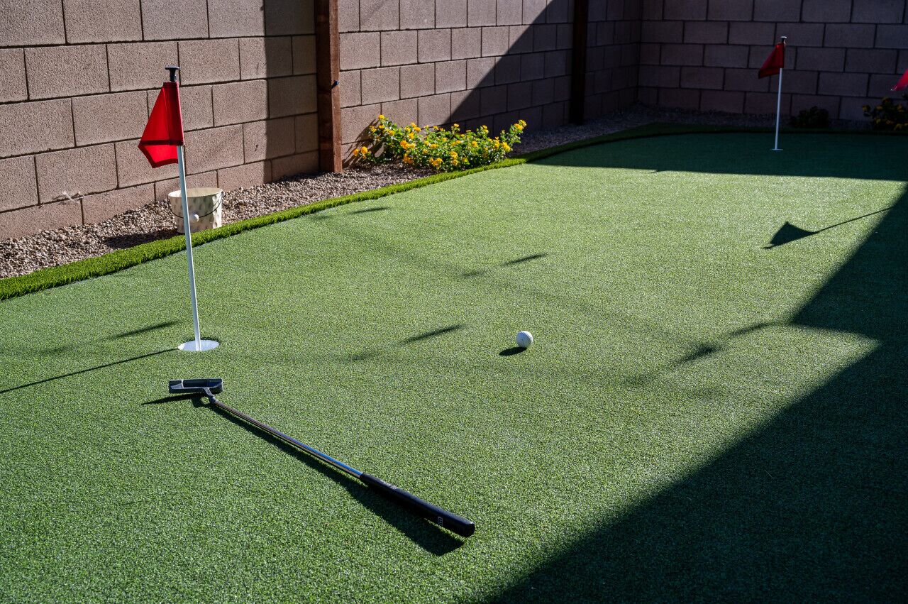 Un campo da minigolf con erba sintetica, una pallina da golf e due bandierelle rosse che segnano le buche.