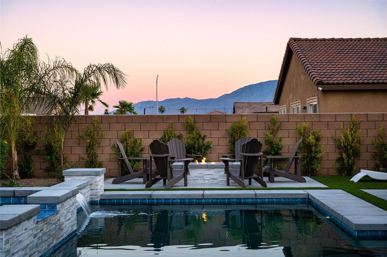 A swimming pool with a fire feature, two Adirondack chairs, and a view of mountains.