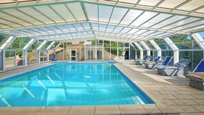 A covered swimming pool with clear glass panels, lounge chairs, and a stone wall in the background. - Hotel La Buca Del Gatto (Cecina)