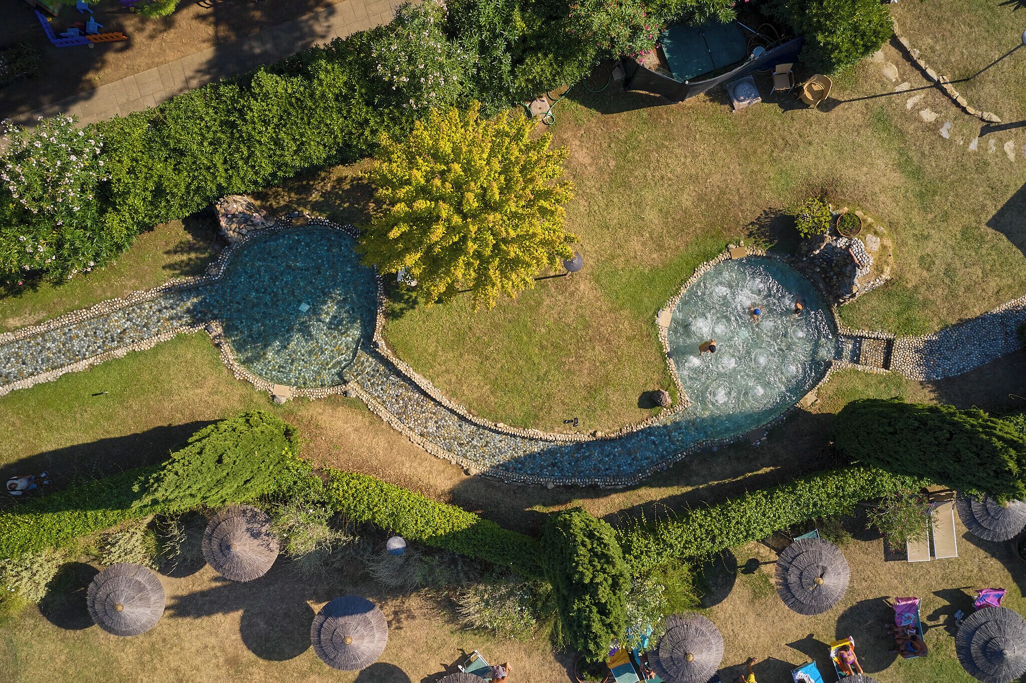 An aerial view of a landscaped area with two circular water features, surrounded by greenery and seating areas.