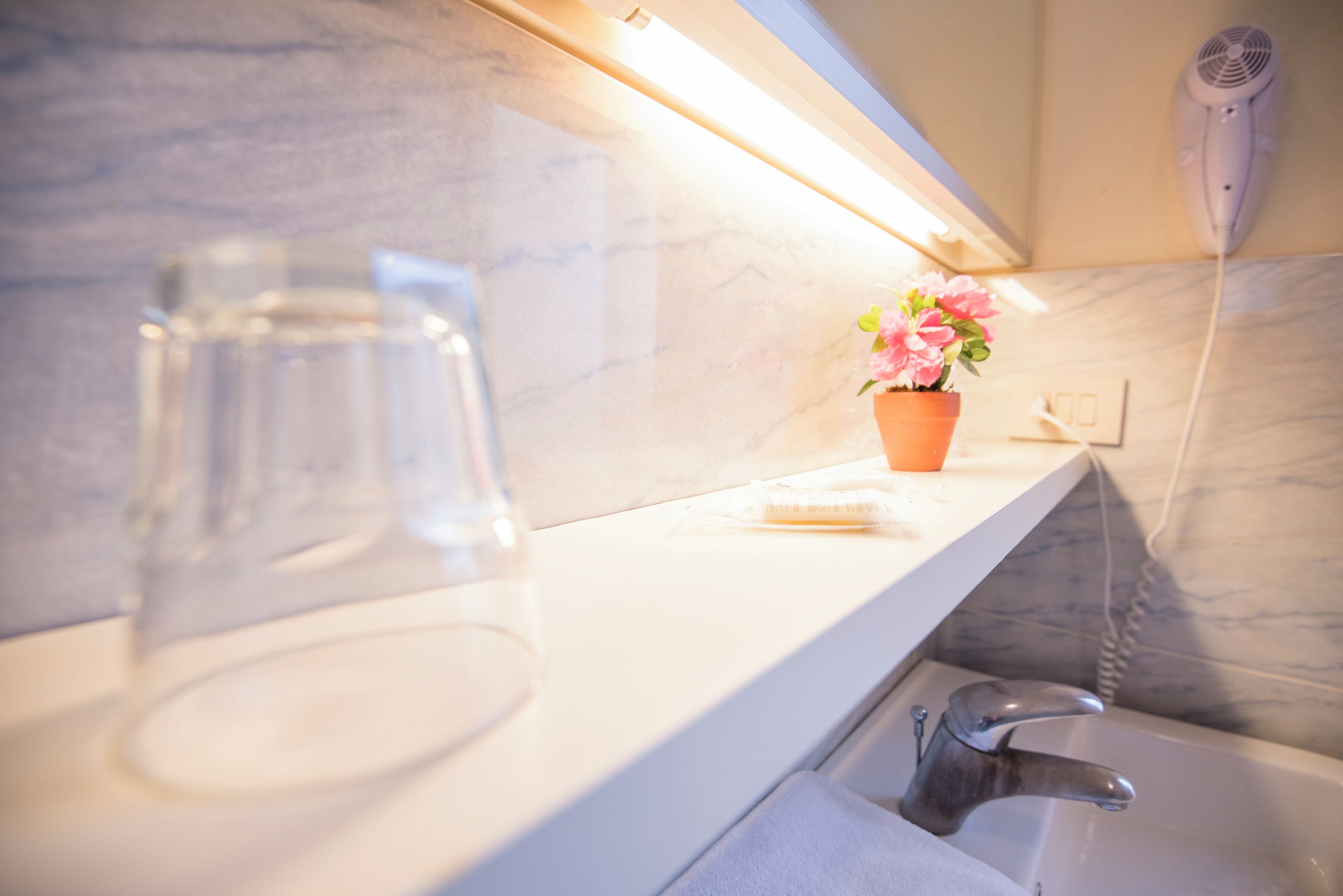 Un bagno con parete in marmo, lavandino, specchio e una pianta in vaso.