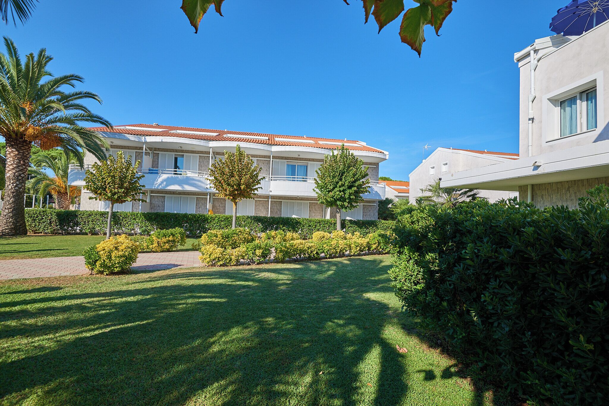 A modern building with a red-tiled roof, surrounded by well-maintained lawns and palm trees.