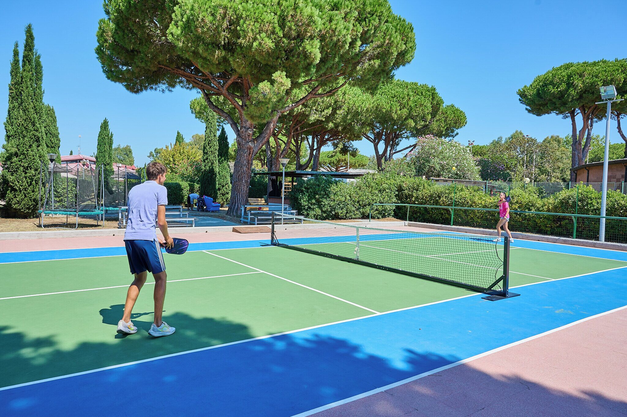 An outdoor tennis court with a net, surrounded by trees and a fence.