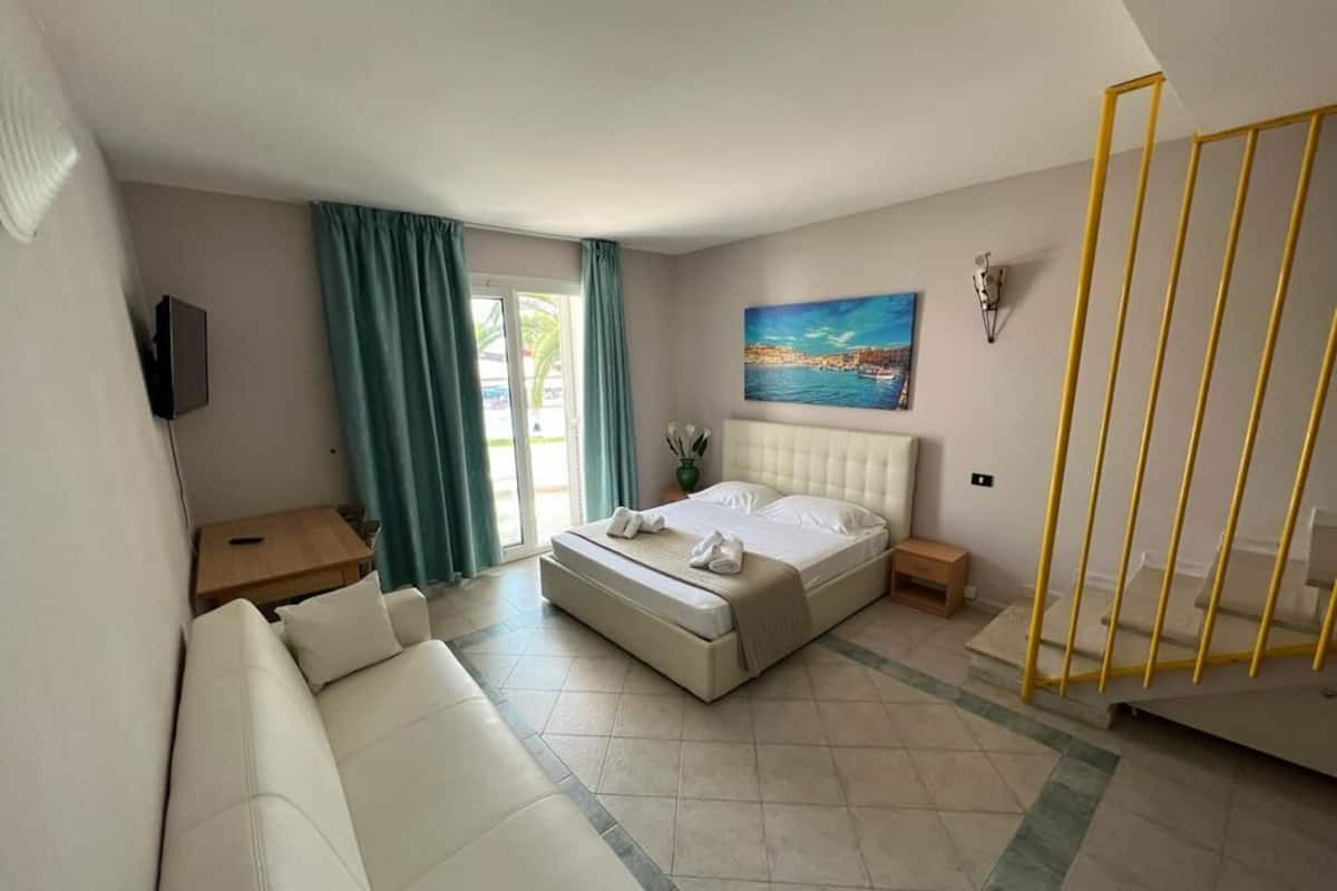A hotel room with a bed, a sofa, a TV, a painting, and a staircase.