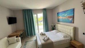 A hotel room with a bed, a TV, a desk, a chair, a sofa, and a painting of a coastal scene. - Hotel La Buca Del Gatto (Cecina)