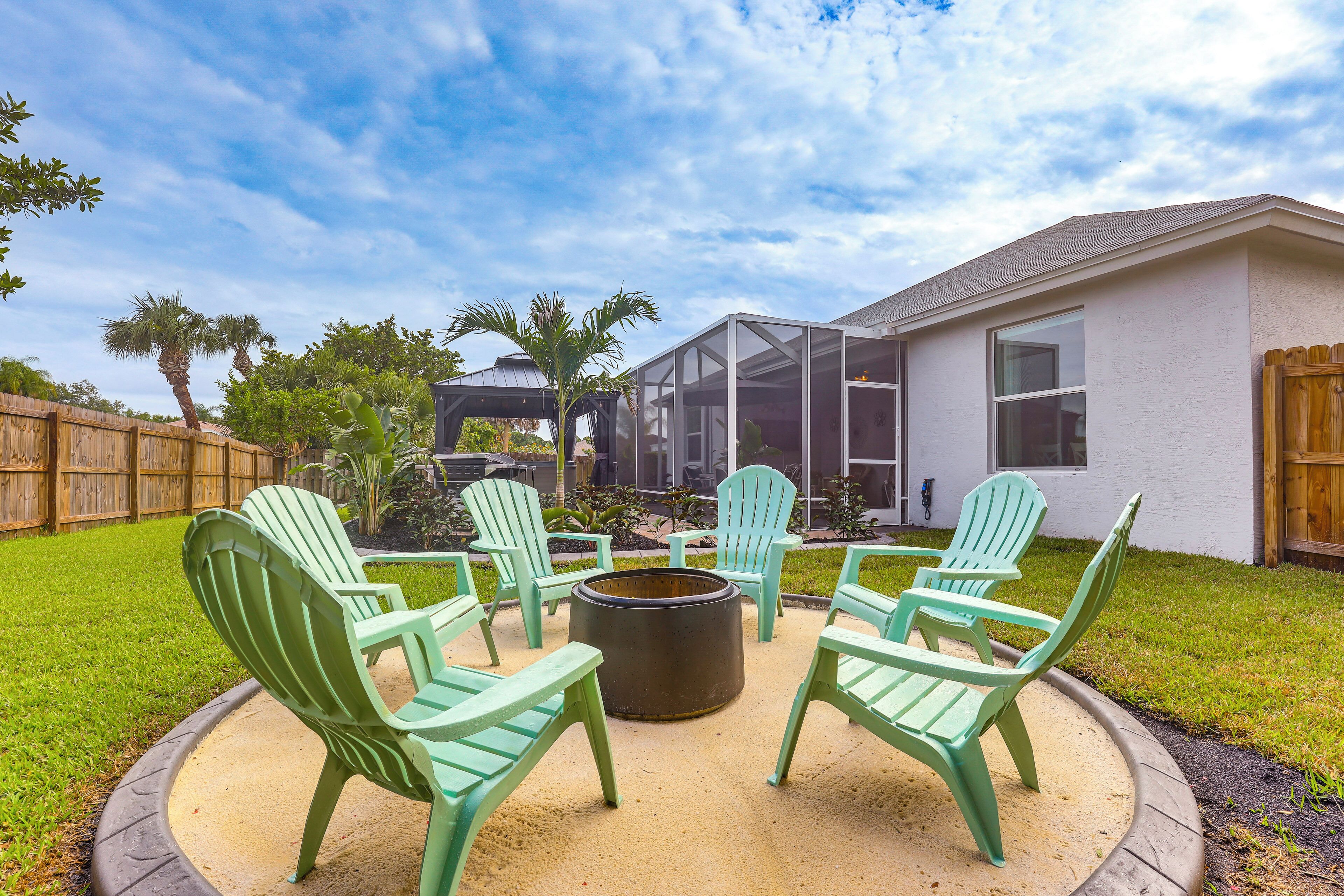Une terrasse dotée de chaises Adirondack vertes et d’un foyer, le tout entouré d’une clôture en bois et de palmiers.