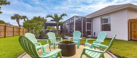 Une terrasse dotée de chaises Adirondack vertes et d’un foyer, le tout entouré d’une clôture en bois et de palmiers.