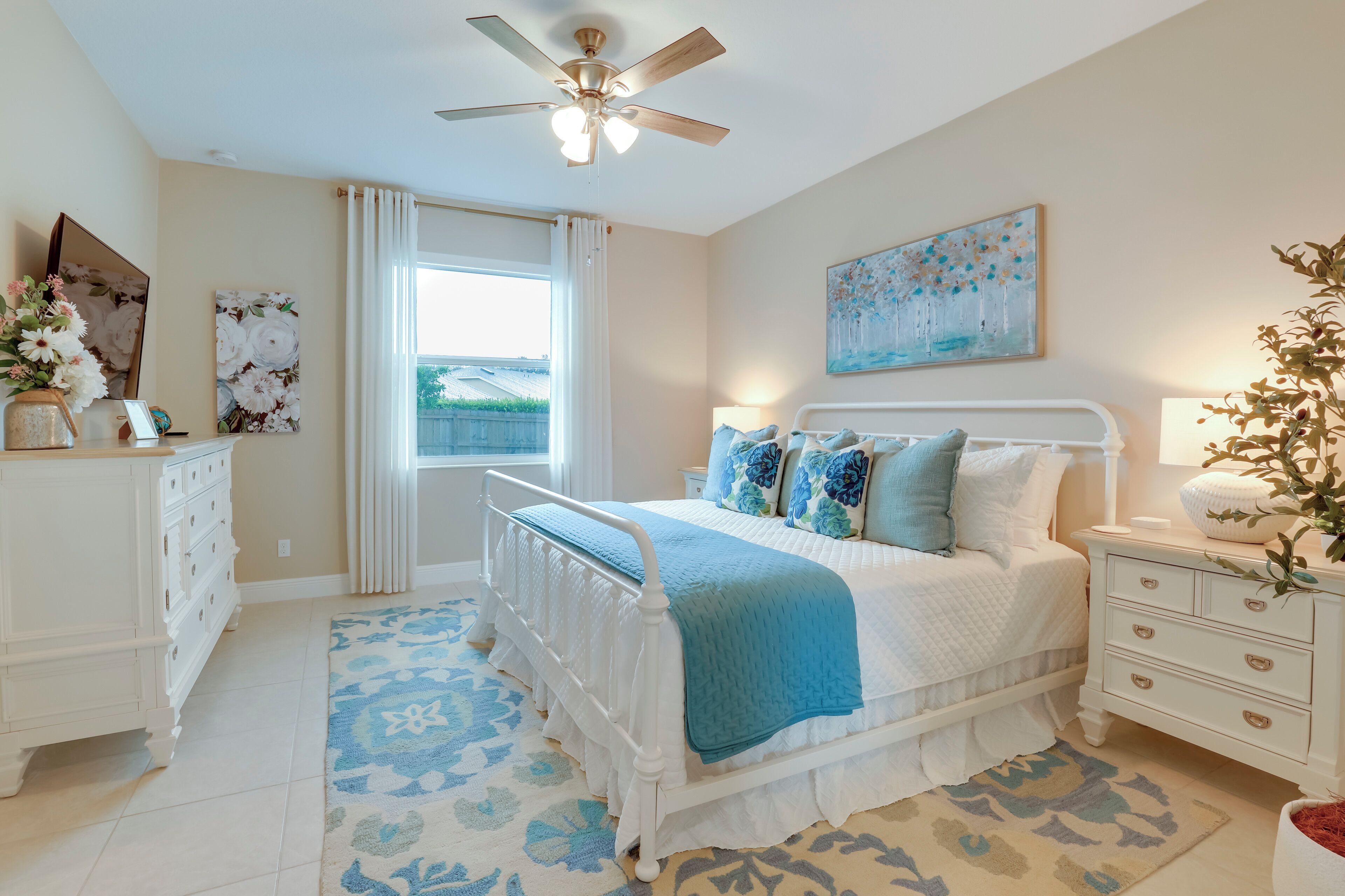A bedroom with a bed, a nightstand, a dresser, a ceiling fan, and a window with curtains.