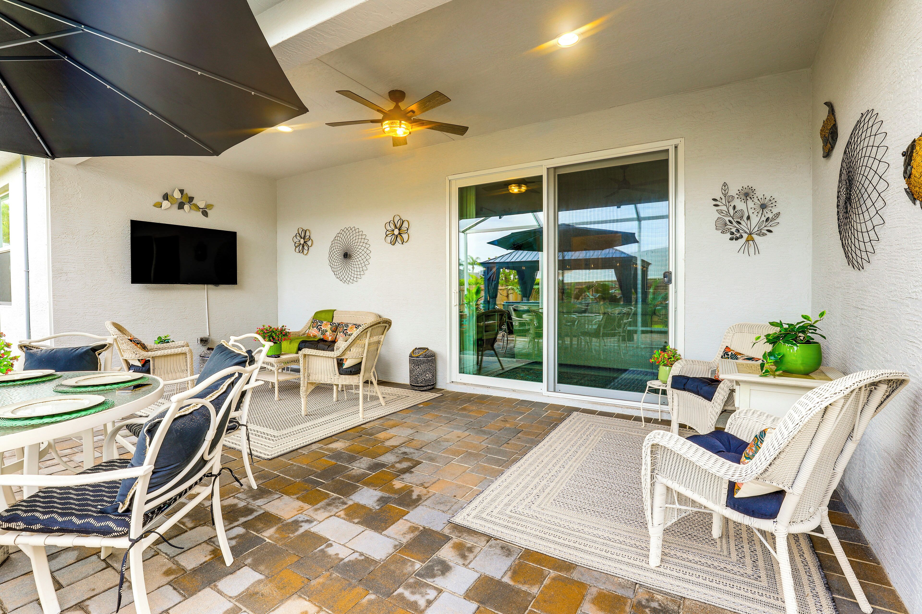 An outdoor patio with wicker furniture, a ceiling fan, and a flat-screen TV mounted on the wall.