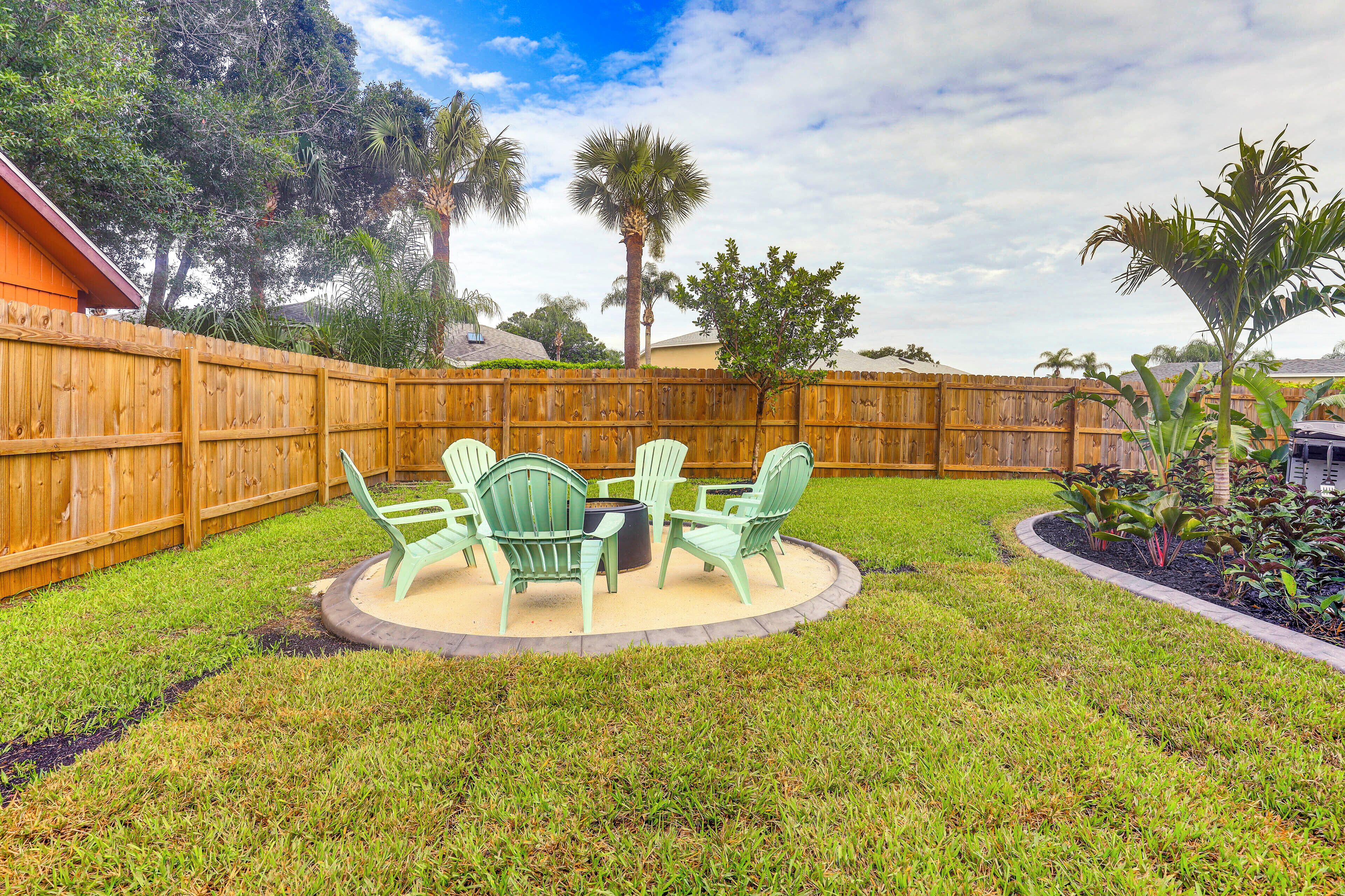 A backyard with a wooden fence, green lawn, and a patio with chairs and a table.