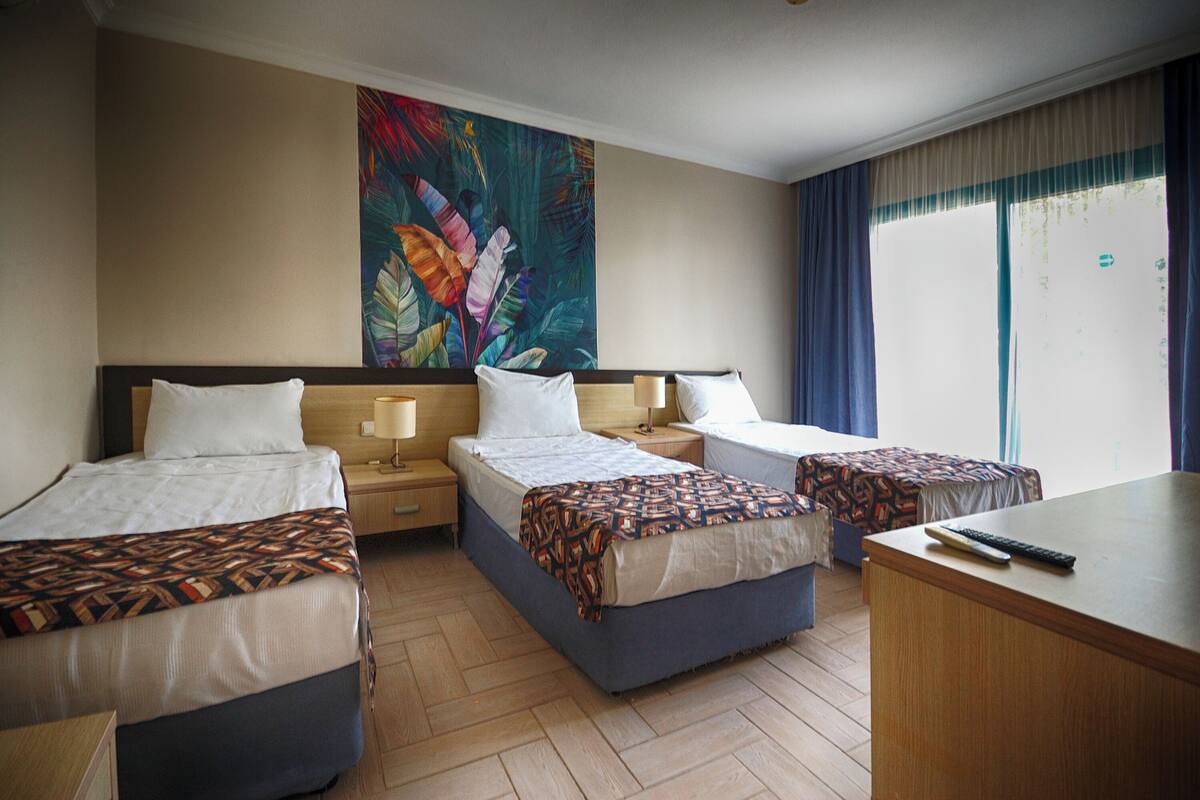 A hotel room with three beds, a desk, and a large window with curtains.