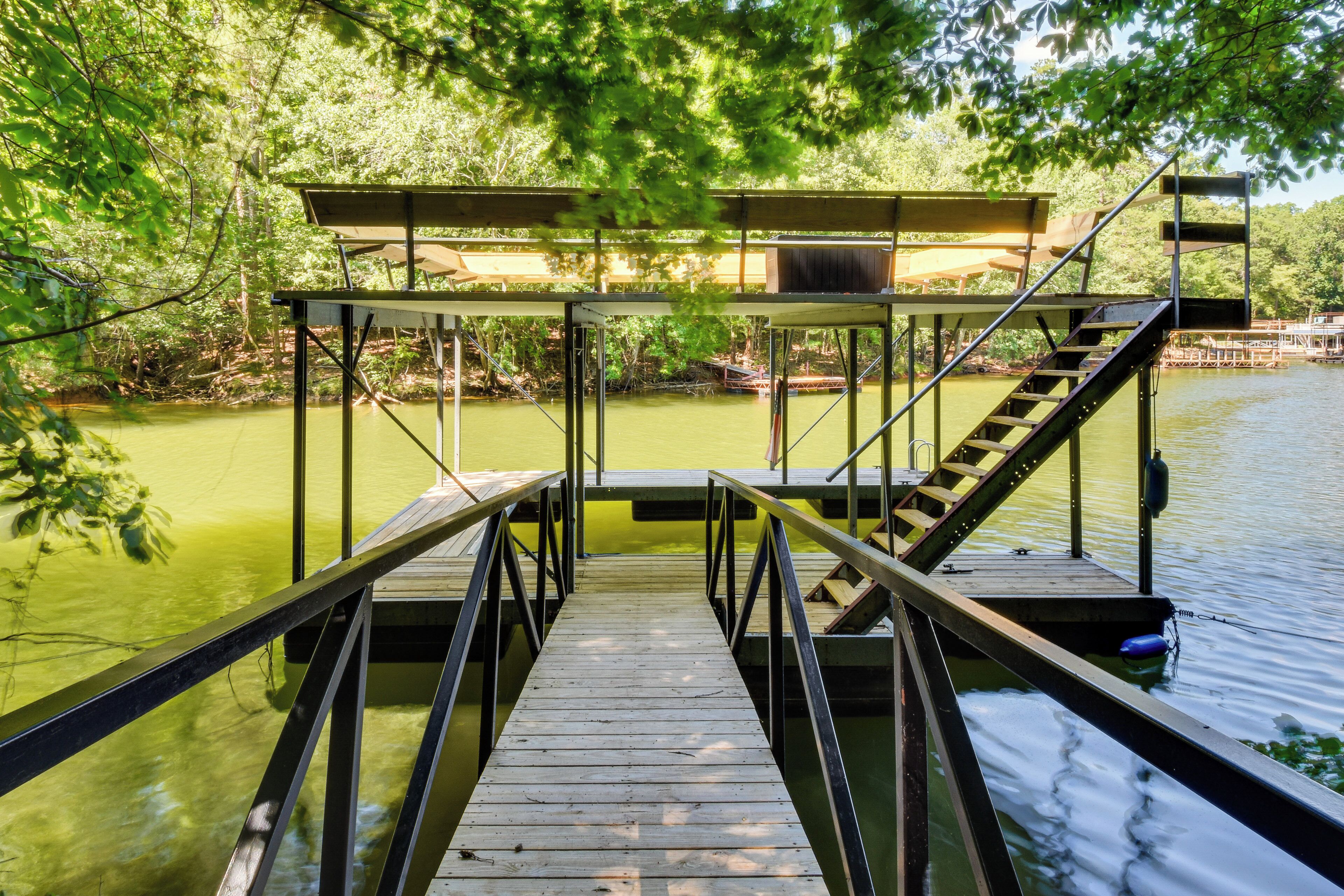 Un muelle de madera que conduce a una zona cubierta con escaleras, rodeado de árboles y agua.