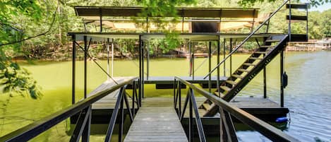 Un muelle de madera que conduce a una zona cubierta con escaleras, rodeado de árboles y agua.
