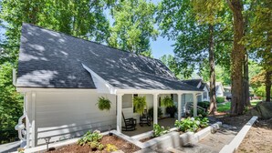 A single-story house with a covered porch, a stone pathway leading to the entrance, and a landscaped garden with various plants and flowers. - Waterfront Gainesville Home w/ Private Boat Dock! (Gainesville)