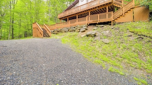 A wooden cabin with a stone foundation, a staircase leading to a balcony, and a gravel path.