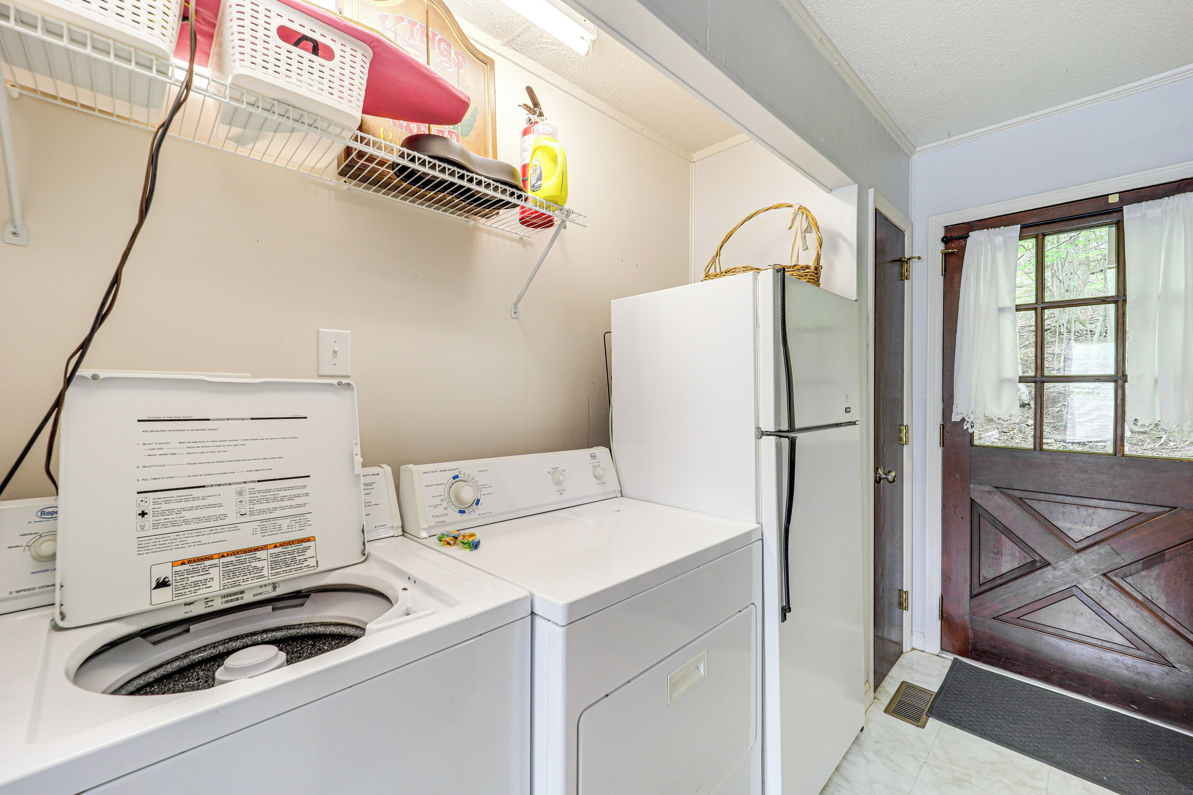A laundry area with a washing machine, dryer, and a shelf with baskets and cleaning supplies.