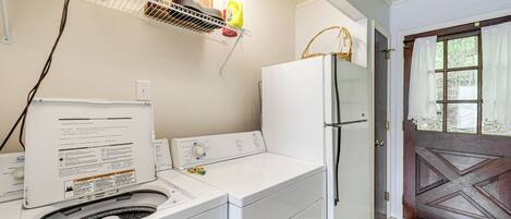 A laundry area with a washing machine, dryer, and a shelf with baskets and cleaning supplies.